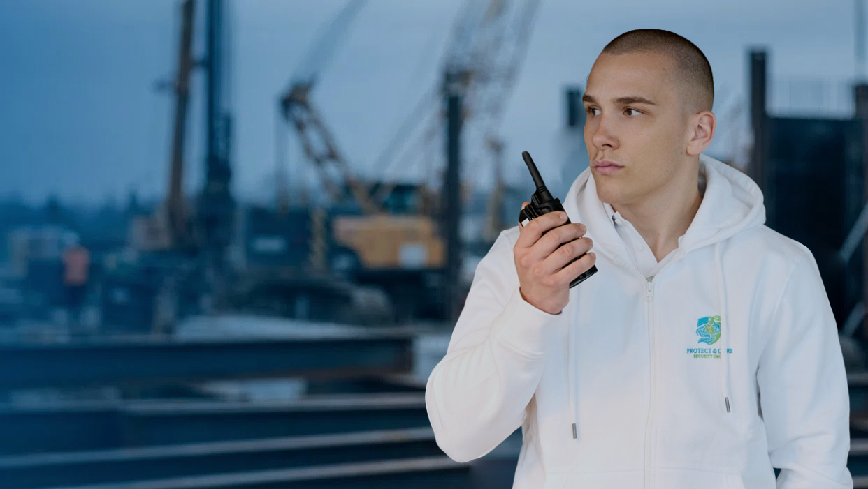 Sicherheitsmitarbeiter mit Funkgerät vor Industriehafen